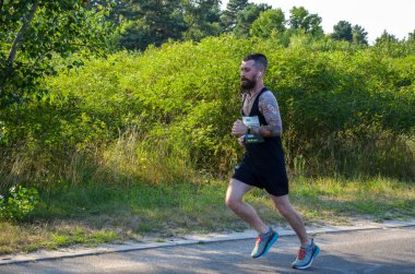 KYIV, UKRAINE - 24 Temmuz 2021: Güneşli yaz gününde asfalt yolda, şehir parkında koşan sağlıklı sporcu. Yaşam tarzı ve spor kavramları