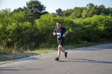 KYIV, UKRAINE - 24 Temmuz 2021: Güneşli yaz gününde asfalt yolda, şehir parkında koşan sağlıklı sporcu. Yaşam tarzı ve spor kavramları