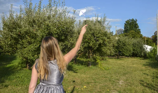 Back view of woman throwing paper airplane against sky outdoors. Travel and open borders concept