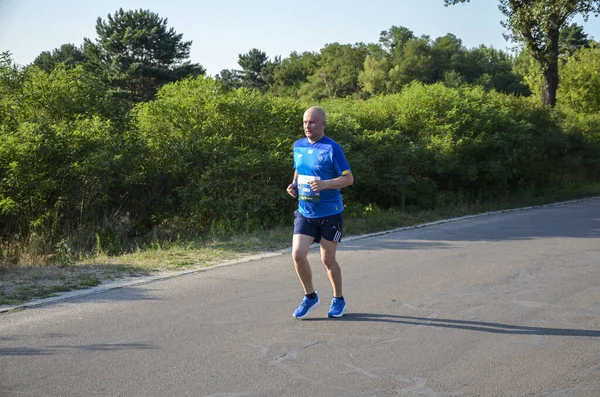 KYIV, UKRAINE - 24 Temmuz 2021: Güneşli yaz gününde asfalt yolda, şehir parkında koşan sağlıklı sporcu. Yaşam tarzı ve spor kavramları