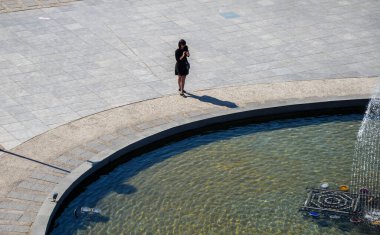 TBILISI, GEORGIA - 14 Ekim 2019: fıskiyenin yanında duran ve akıllı telefonunu kullanan siyah elbiseli yalnız bir kızın üst görüntüsü. Toplantı için bekliyorum.