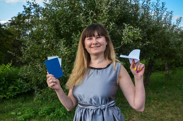 Smiling pretty woman with air tickets and international passport and paper plane in hand, dreaming to going abroad. Travel and vacation