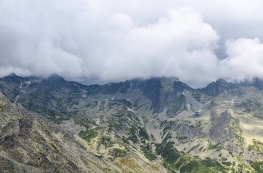 Slovakya 'daki Ulusal Park High Tatras' ta dağ sıraları, zirveleri, gölleri ve düşük beyaz bulutları olan kayalık bir manzara.