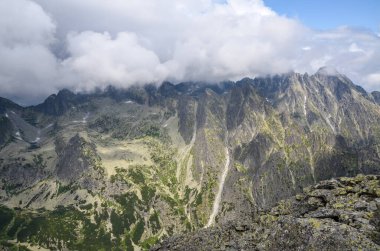 Slovakya 'daki Ulusal Park High Tatras' ta dağ sıraları, zirveleri, gölleri ve düşük beyaz bulutları olan kayalık bir manzara.