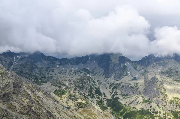 Slovakya 'daki Ulusal Park High Tatras' ta dağ sıraları, zirveleri, gölleri ve düşük beyaz bulutları olan kayalık bir manzara.