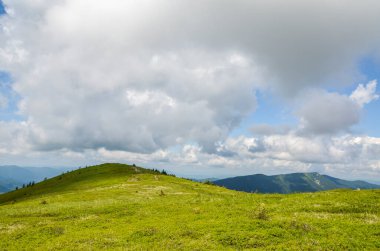 Tepelerinde yemyeşil çimenler ve arka planında bulutlu mavi gökyüzü olan güzel dağ sırtı. Karpatlar, Ukrayna