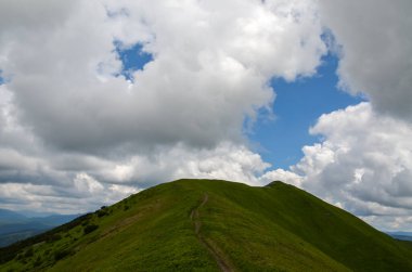 Dağlık dağ manzarası, patika ve yeşil çayır, çimenli tepeler ve bulutlu gökyüzüne karşı orman. Karpat Dağları, Ukrayna