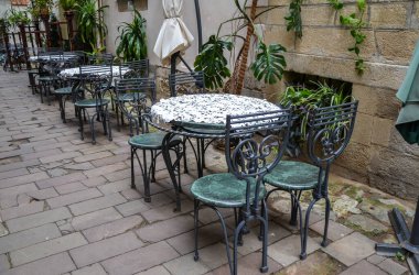 Eski şehir caddesindeki yazlık kafe terasında boş yuvarlak masalar ve sandalyeler.