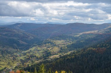 Picturesque autumn scenery village in the mountain slopes with colorful trees and meadows. Carpathian Mountains, Ukraine
