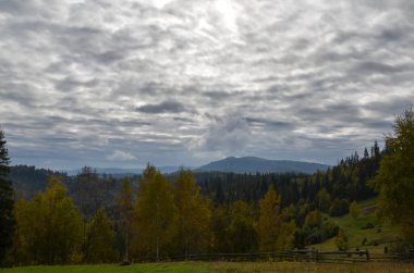 Bulutlu gökyüzünün altındaki renkli ormanlı sonbahar dağ manzarasının manzarası. Karpat Dağları, Ukrayna