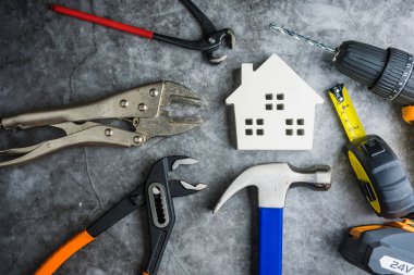 Ahşap beyaz ev oyuncakları ve inşaat aletleri. Gri-siyah çimento zemin zemininde kopya alanı var. Emlak konsepti, yeni ev onarım konsepti.