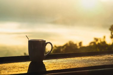 Pha Chang Noi, Tayland 'ın Phayao bölgesindeki bulanık dağ zemininin üzerindeki ahşap balkon korkuluklarına bir fincan kahve kapatın..
