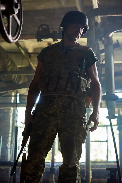 A Ukrainian soldier in a helmet and body armor stands in a house destroyed by a bomb.