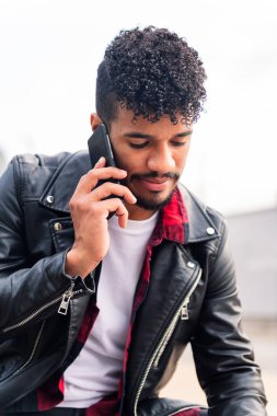 telefonda konuşan genç ve şık bir Latin adamın dikey portresi, teknoloji kavramı ve şehir yaşam tarzı