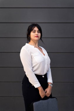 serious businesswoman looking at camera holding briefcase, concept of successful entrepreneur and urban lifestyle