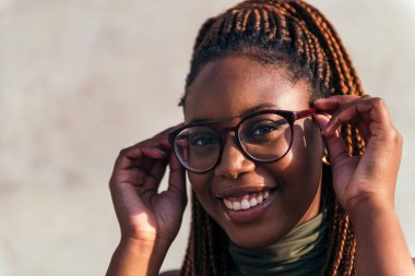 Gözlüğünü takıp kameraya, gençlik konseptine ve ırksal çeşitliliğe bakan gülümseyen siyahi bir kadının yakın plan portresi.