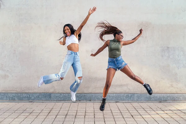 灰色のコンクリートの壁を背景に友情と都市生活の概念で幸せなジャンプ2人の若い黒人の女の子 — ストック写真