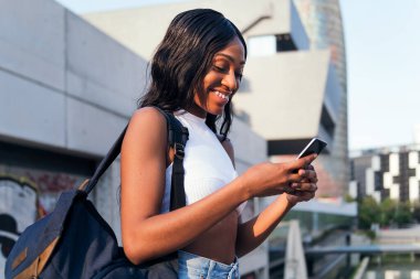 Sırt çantası gülüşlü genç Afrikalı kız cep telefonuna, gençlik konseptine ve şehir yaşam tarzına danışıyor.
