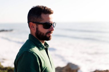 Deniz kenarında güneş gözlüklü çekici bir adamın portresi, rahatlama ve rahatlama konsepti, metin için yer kopyalama