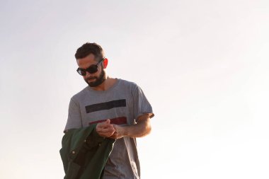 Güneş gözlüklü yakışıklı adam ceketini çıkartıyor. Arka planda gökyüzü, rahatlama ve rahatlama kavramı, metin için kopyalama alanı.