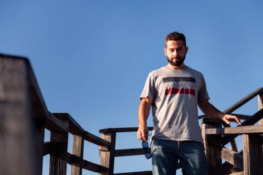 Çekici genç bir adam arka planda mavi gökyüzü olan ahşap bir merdivenden iniyor, boş zaman kavramı ve rahatlama, metin için kopyalama alanı