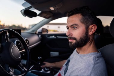 çekici sakallı genç adam arabasının direksiyonunda oturuyor, boş zamanı ve sürüş konsepti