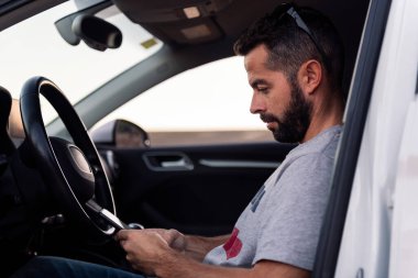 Çekici sakallı genç adam cep telefonunu kullanıyor. Arabasında dinleniyor. Boş vakitleri ve iletişim teknolojisi kavramını kullanıyor.