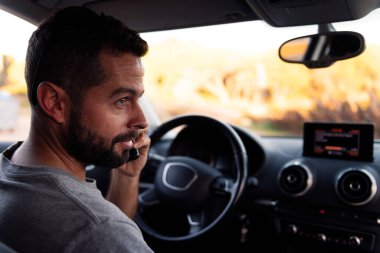 Yakışıklı sakallı genç adam arabasının içinde oturmuş beklerken cep telefonuyla konuşuyor. Boş vakit ve iletişim teknolojisi kavramı.