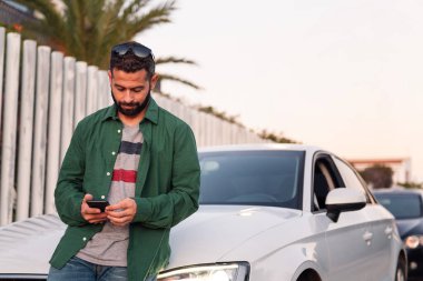 çekici genç sakallı adam araba kaputunda oturuyor cep telefonuna danışmanlık, eğlence ve iletişim teknolojisi konsepti, metin için kopyalama alanı