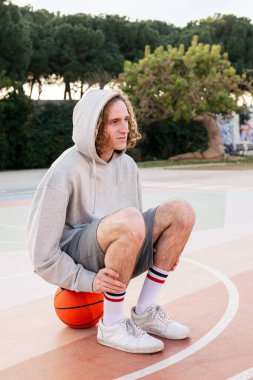 Basketbol oynadıktan sonra sahada oturan beyaz bir adam, şehir sporu kavramı.