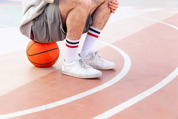 Benen Van Een Onherkenbare Man Zittend Een Bal Het Basketbalveld — Stockfoto