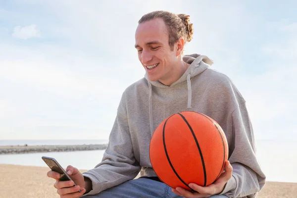 Młody Biały Mężczyzna Kapturze Koszykówce Uśmiechnięty Pomocą Telefonu Komórkowego Koncepcja — Zdjęcie stockowe