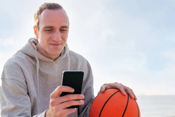 Smiling Caucasian Man Hoodie Basketball Using His Mobile Phone Concept — ストック写真