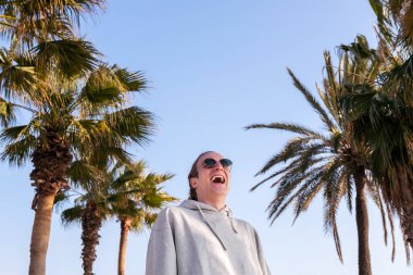 Güneş gözlüklü beyaz adam kahkahalarla gülüyor.