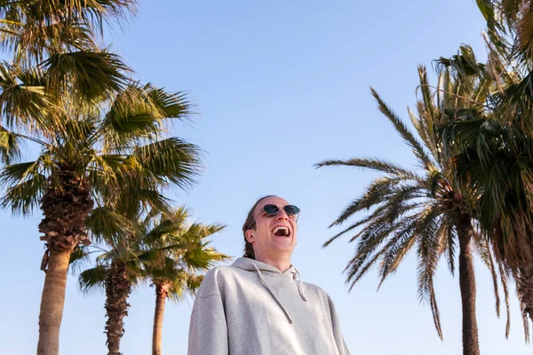 Güneş gözlüklü beyaz adam kahkahalarla gülüyor.