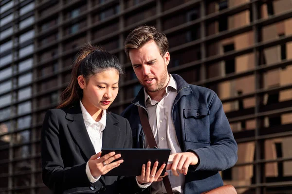 young entrepreneur woman showing her tablet to a businessman next to an office building in the financial district, concept of entrepreneurship and business