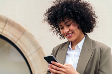 Kıvırcık saçlı genç bir kadının portresi mutlu bir şekilde cep telefonu, gençlik ve teknoloji konsepti ile mesaj yazıyor, metin için kopyalama alanı