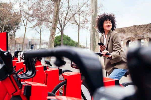 Sorrindo Jovem Latina Usando Seu Telefone Enquanto Sentada Uma Bicicleta — Fotografia de Stock