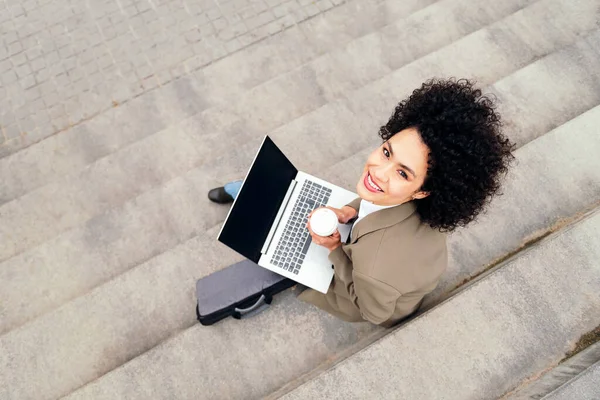 top view of a smiling woman working with laptop computer sitting outdoors on a staircase, concept of business and urban lifestyle, copy space for text