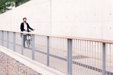 young caucasian man wearing trendy clothes and walking in front of a white wall with his bike, concept of urban lifestyle and sustainable mobility, copy space for text