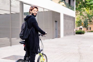 smiling young man wearing trendy clothes and walking with his folding bike in the city, concept of urban lifestyle and sustainable mobility, copy space for text