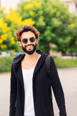 vertical portrait of a stylish young man with beard and sunglasses smiling happy looking at camera, concept of youth and urban life style, copy space for text