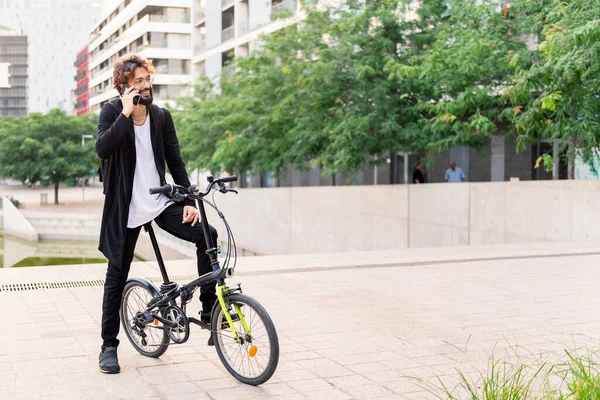 young caucasian man smiling happy talking on his mobile phone while sitting on his bike in the city, concept of technology of communication and sustainable mobility, copy space for text