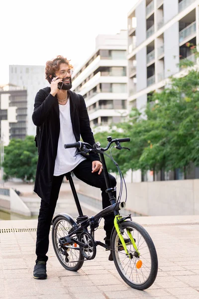young caucasian man smiling happy talking on his mobile phone while sitting on his bike in the city, concept of technology of communication and sustainable mobility