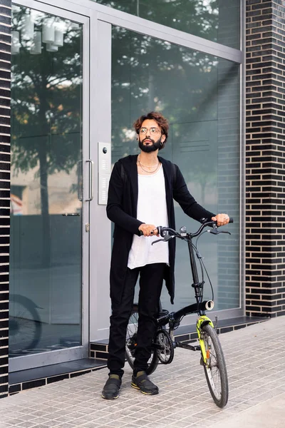 young caucasian man leaving his front door walking with his bike, concept of urban lifestyle and sustainable mobility