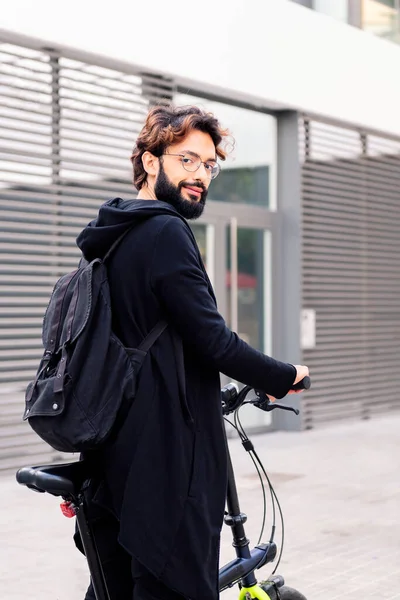 smiling young man wearing trendy clothes and walking with his folding bike in the city, concept of urban lifestyle and sustainable mobility