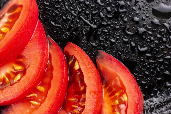 Pomidor w plasterkach. Kawałki pomidora na czarnej tabliczce. — Zdjęcie stockowe