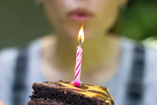 A burning candle in a piece of chocolate cake. Blow out the candle and make a wish. High quality photo