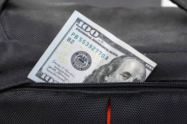 A hundred dollar bill peeks out from the pocket of a bag. Open pocket. Zipped pocket. High quality photo