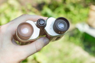 Binoculars in the hands of a traveler. Sun glare on binocular lens. Exploration of the surrounding area. High quality photo